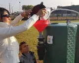 Une femme verse des déchets organiques dans un entonnoir rouge, alimentant un méthaniseur domestique. Un garçon regarde, curieux.