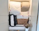 Ordentlich verstaut: weiße Bettdecke falten und Kissen im Schrank, daneben eine Decke und ein Korb mit Bettzeug.