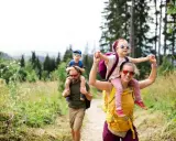 Rodzina wędruje po górach, dzieci siedzą na karkach rodziców. Wspaniały długi weekend sierpnia w otoczeniu natury.