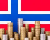 Stosy monet na tle flagi Norwegii symbolizują oszczędności i przyszłość, być może związane z wiekiem emerytalnym w Norwegii.