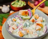Ein Löffel mit einem Stück Hähnchen, Gurke und roter Zwiebel, bereit, in einen cremigen Salat zu tauchen. Perfekt für proteinreiche Salate!
