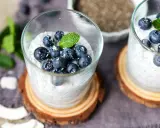 Zwei Gläser mit cremigem Chia Pudding, garniert mit Blaubeeren, Kokosraspeln und Minze. Ein gesunder Genuss!