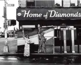 Corky Lee photos: A person in ornate robes stands beside a Statue of Liberty cutout on a wet street, with "Home of Diamonds" sign above.