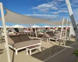 Un lido a Riccione con lettini doppi e ombrelloni bianchi sotto un cielo azzurro e nuvoloso.