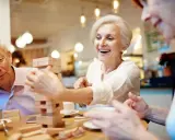 Anziani ridono giocando a Jenga, un esempio di iniziative per anziani che promuovono divertimento e socialità.
