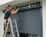 Fachowiec na drabinie dokonuje naprawy rolety zewnętrznej, regulując mechanizm w kasecie.