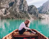 Uśmiechnięta kobieta w łodzi na turkusowym jeziorze w **Włoszech Dolomity**. Majestatyczne góry i lasy tworzą tło dla tej malowniczej sceny.