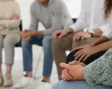 Grupa osób siedzi w kręgu, wspierając się nawzajem. To obraz nadziei i wspólnej drogi w terapii od uzależnień.