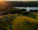Malownicze domki glampingowe nad jeziorem, idealne na wakacje. Słońce zachodzi, tworząc złote światło na polach i lasach.