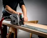 Main d'un artisan guidant une scie circulaire sur un rail pour une coupe précise sur une planche de bois.