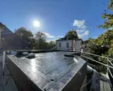 Ein frisch abgedichtetes Flachdach unter strahlender Sonne. Die Dachhaut glänzt, zwei Dachfenster sind sichtbar.