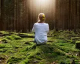 Frau sitzt im Wald auf moosbewachsenem Boden, sucht Ruhe, wenn sie immer gestresst und genervt ist.