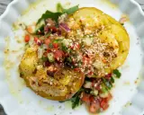 Kumpir rezept: Zwei gebackene Kartoffelhälften, gefüllt mit Käse und belegt mit frischem Tomaten-Gurken-Salat und Sesam.