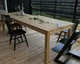 Ett träbord och stolar på en altan. Bordet är dekorerat med blommor och ljus. Perfekt för att behandla furu utomhus och njuta av sommaren.
