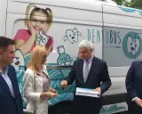 Ludzie stojący przed białym Dentobusem z grafikami uśmiechniętych zębów i dziewczynki.
