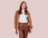 Donna sorridente con un elegante outfit con pantaloni di pelle larghi marroni, dolcevita bianco e cappotto cammello.
