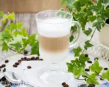 Jak zrobić latte? Warstwowy napój kawowy w szklance, otoczony bluszczem i ziarnami kawy.