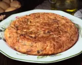 Tortilla española, un clásico de la comida típica de Granada, servida en un plato decorado. Patatas y aceite en el fondo.