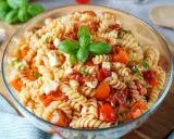 Ein köstlicher mediterraner Nudelsalat mit Fusilli, Kirschtomaten, Mozzarella-Würfeln und frischem Basilikum, garniert mit einem Basilikumblatt.
