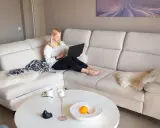 Mujer rubia trabajando en su portátil en un cómodo sofá beige. Es un lugar perfecto para relajarse y ser productivo.