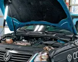 Pod maską niebieskiego VW z silnikiem 2.0 TDI, mechanik oświetla silnik lampą.