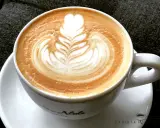 Eine Tasse Cappuccino mit kunstvoller Barista Art, die ein Herz und Blätter zeigt.