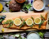 Flammlachs mit Zitronenscheiben und Dill, serviert mit cremigen Dips und frischem Salat als Beilagen.