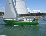Un voilier vert vif navigue sur l'eau, avec un autre bateau à moteur en arrière-plan. Une belle journée pour une croisière, peut-être avec une dégustation d'armagnac à bord de ce bateau.