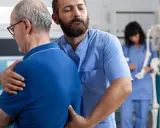 Fizjoterapeuta pomaga starszemu mężczyźnie, który odczuwa ostry ból kręgosłupa lędźwiowego. W tle widać szkielet i drugą pielęgniarkę.