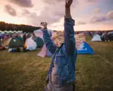 Ragazza con le braccia alzate in un campo di tende, immersa nell'atmosfera di uno dei festival techno più famosi.