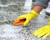 Ręce w żółtych rękawiczkach szorują szczotką płomieniowany granit, usuwając brud i pianę.