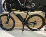 Czarny rower z żółtymi akcentami, wyposażony w baterię i silnik, prezentuje tani zestaw do konwersji roweru na elektryczny.