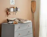 Eine Wickelkommode organisieren: Spielzeug, Handtücher und Pflegeutensilien sind ordentlich verstaut. Ein Holzpaddel lehnt an der Wand.