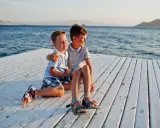 Dos niños sonríen sentados en un muelle blanco. ¡Ideas para que hacer en Murcia con niños!