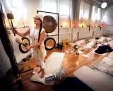 En kvinna spelar gong för en grupp liggande deltagare. Ljudvågorna sprider sig som **ra ma da sa** och skapar en lugn atmosfär.