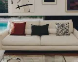 Sofá blanco con cojines decorativos: uno rojo, uno verde con textura y otro con estampado de cebra.