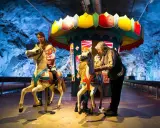 Familj njuter av en karusell i en grottliknande miljö på Stockholm Toy Museum.