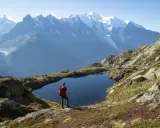 Widok na wejście na Mont Blanc. Turysta z plecakiem i kijkami stoi nad górskim jeziorem, podziwiając ośnieżone szczyty.