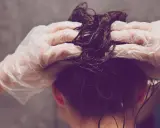 Hände mit Handschuhen tragen Olaplex Nr. 3 auf nasses, dunkles Haar auf.