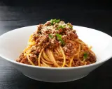 Pyszny makaron z mięsem mielonym, posypany parmezanem i natką pietruszki, podany w białej misce.