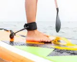 Noga na desce SUP z leash'em, niezbędne akcesoria do sup dla bezpieczeństwa. Wiosło w tle.