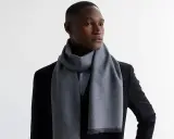 Elegancki mężczyzna w czarnym garniturze i błękitnej koszuli, z szarym szalikiem męskim przewiązanym wokół szyi.