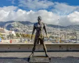 Bronzestatue von Cristiano Ronaldo am Hafen von Funchal, Madeira. Hinter ihm erstreckt sich die Stadt bis zu den Bergen. Ein Denkmal für den weltberühmten Fußballer, das man fast wie am **cristiano ronaldo flughafen** erwarten könnte.