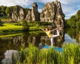 Frau praktiziert Yoga am See vor den Externsteinen NRW. Die Felsen spiegeln sich im Wasser.