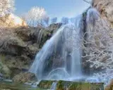 Cascada helada en el nacimiento del río Júcar, con ramas cubiertas de escarcha y agua cayendo sobre rocas.