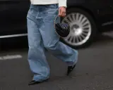 Spodnie baggy damskie stylizacje: luźne jeansy, biały sweterek i czarna torebka z łańcuszkiem.