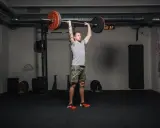 Mann führt einen **strict press** mit einer Langhantel im Fitnessstudio aus.
