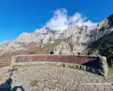 Impresionante mirador de los Picos de Europa con un muro de piedra y metal decorado. El sol ilumina las majestuosas montañas.