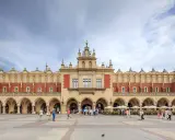 Sukiennice w Krakowie, zabytkowy budynek z arkadami, tętni życiem. Ludzie spacerują po Rynku Głównym, podziwiając architekturę.