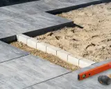 Budowa tarasu z bloczków betonowych w piasku. Poziomica i młotek czekają na dalsze prace.